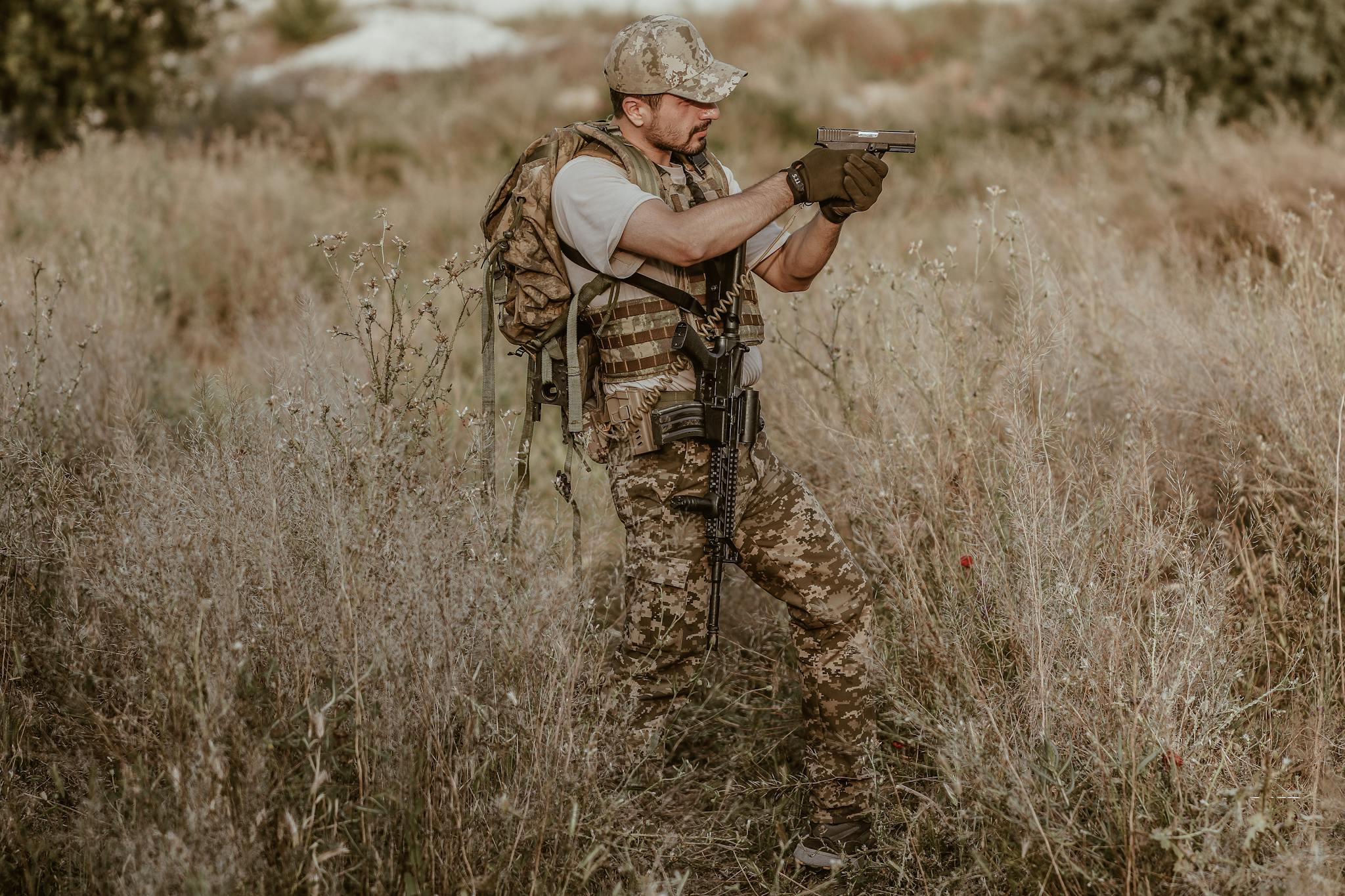 A camouflaged soldier aiming a weapon in a grassy field, ready for action.